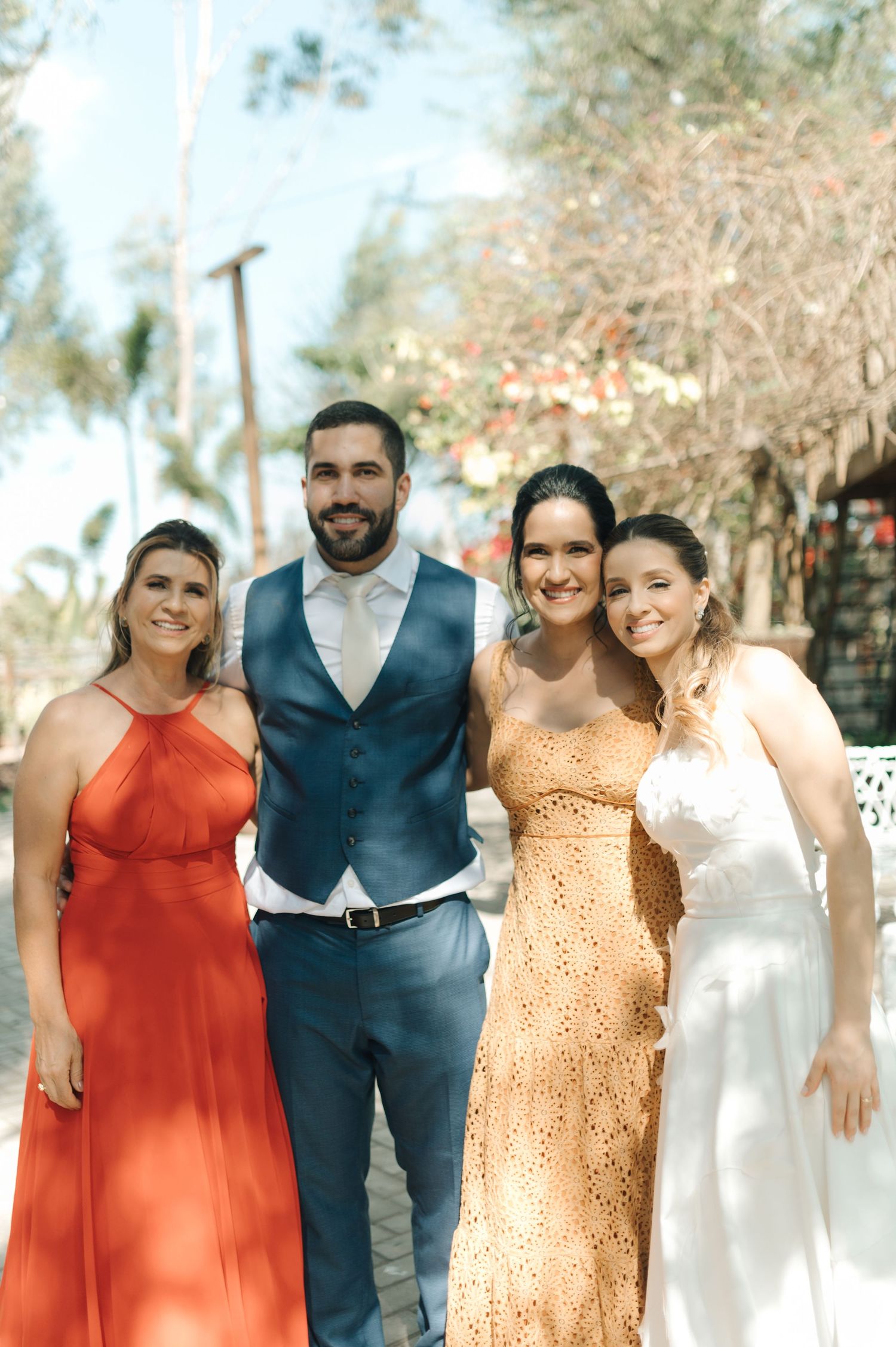 A group poses together outdoors wearing formal attire in coral, blue and white tones.