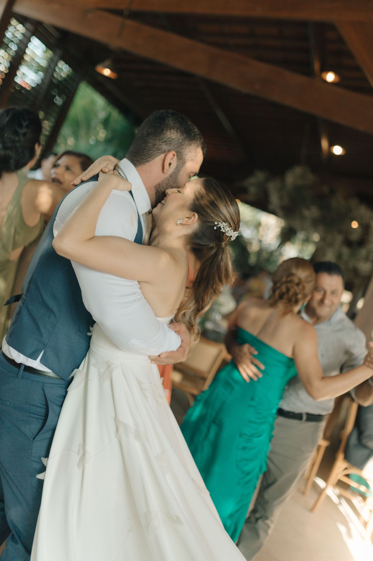 A couple shares their first dance while guests watch in an outdoor covered venue.