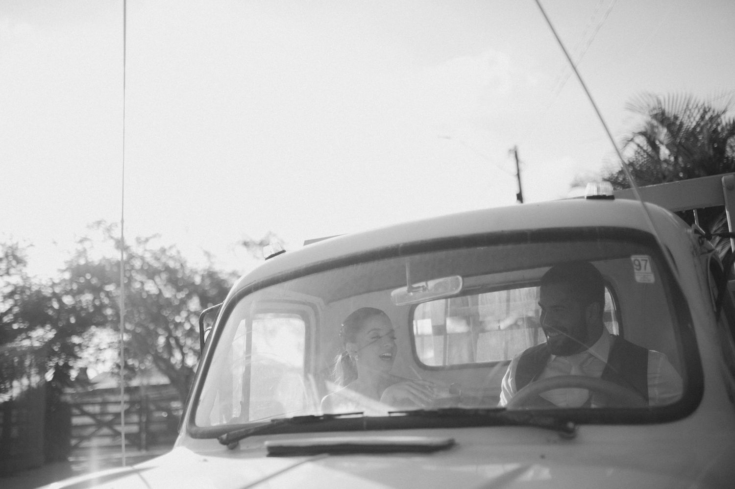 A black and white photo of newlyweds sharing a moment inside a vintage vehicle.