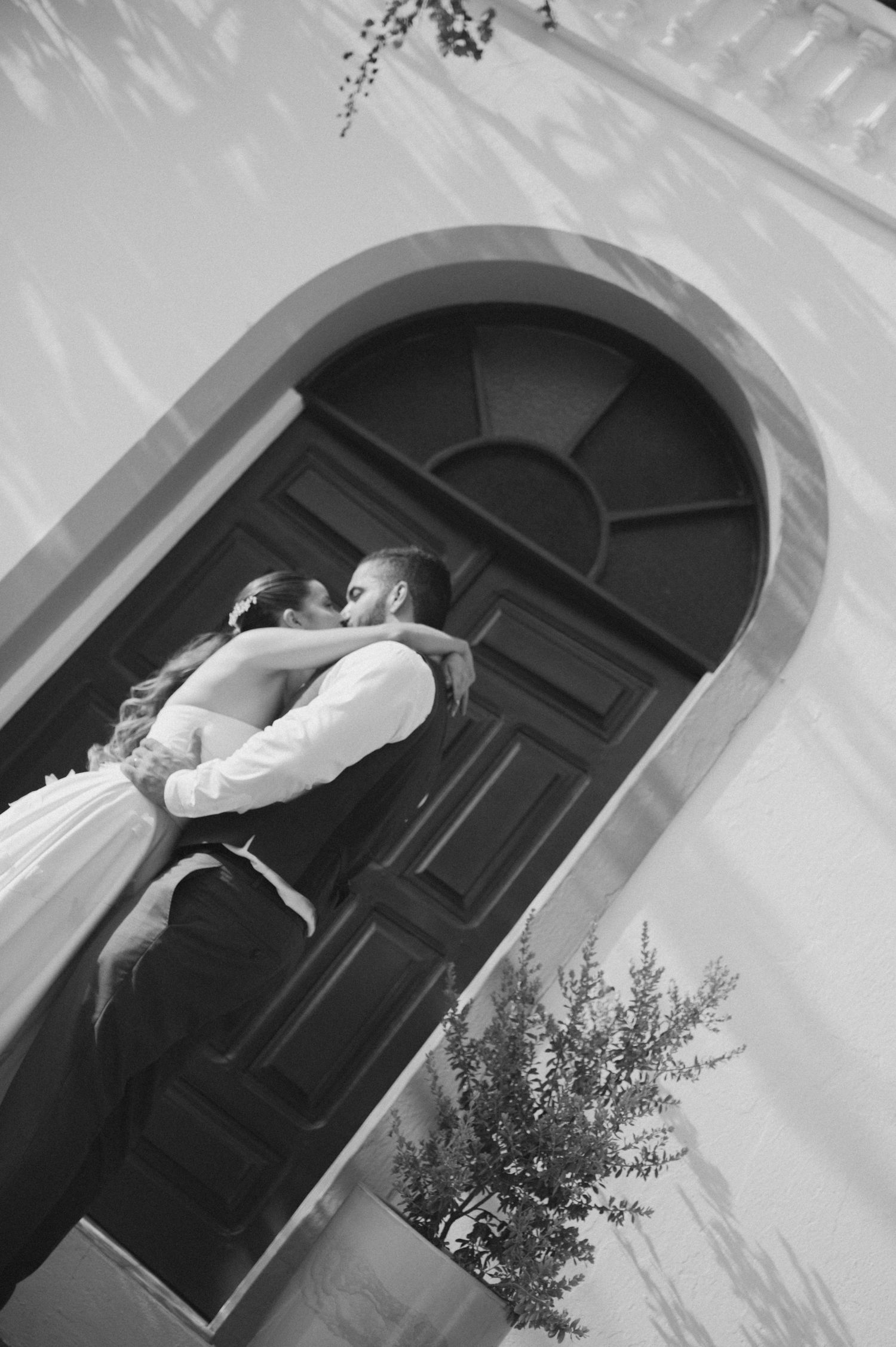 A romantic black and white wedding photo of a couple embracing under an arched doorway.