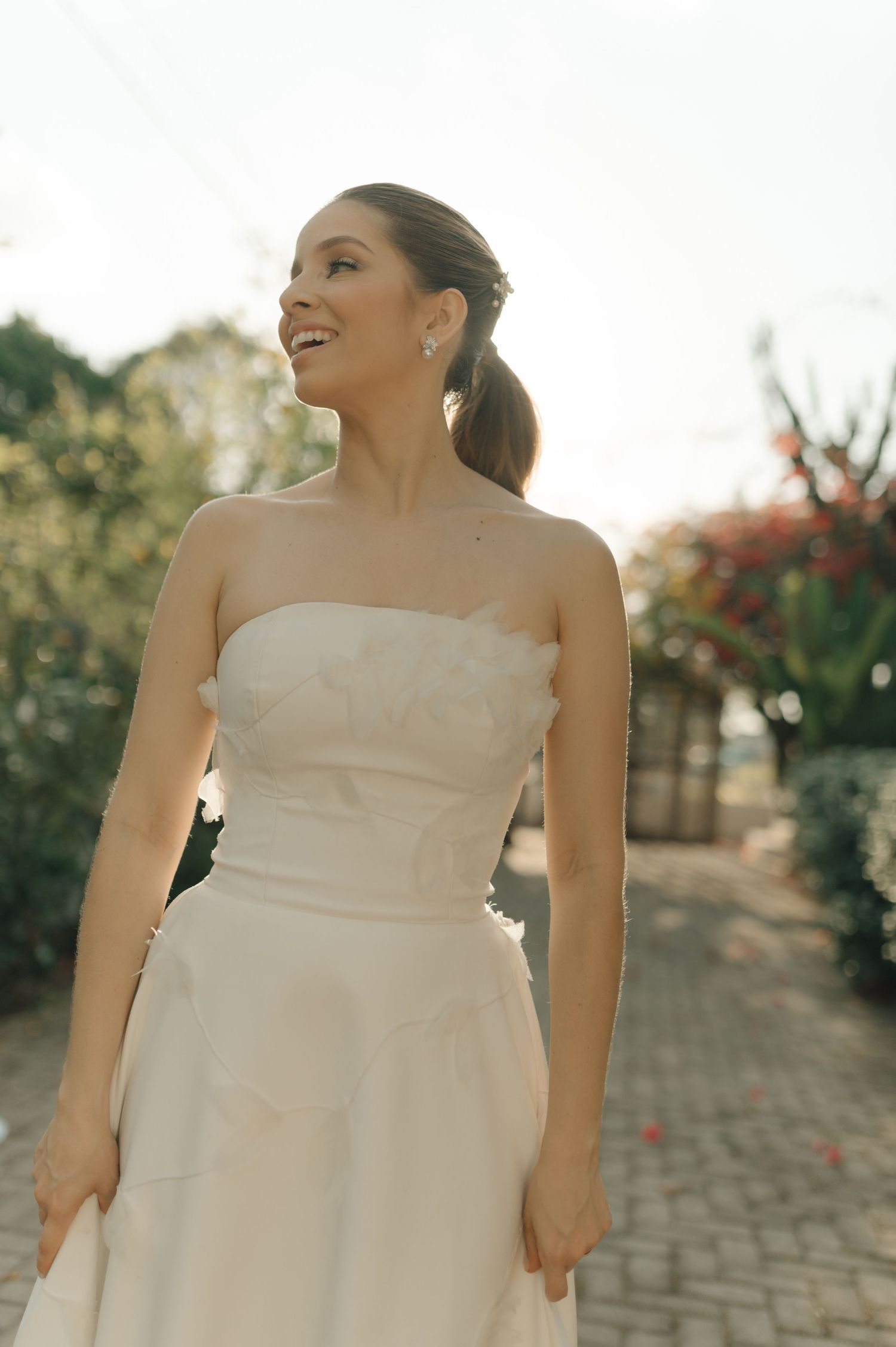 Bride in a strapless white wedding gown poses in a garden setting.