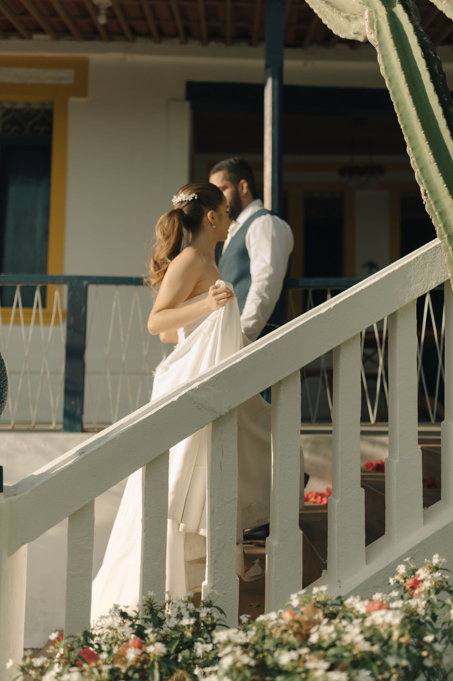 Romantic wedding moment captured on a white porch with blooming flowers below.