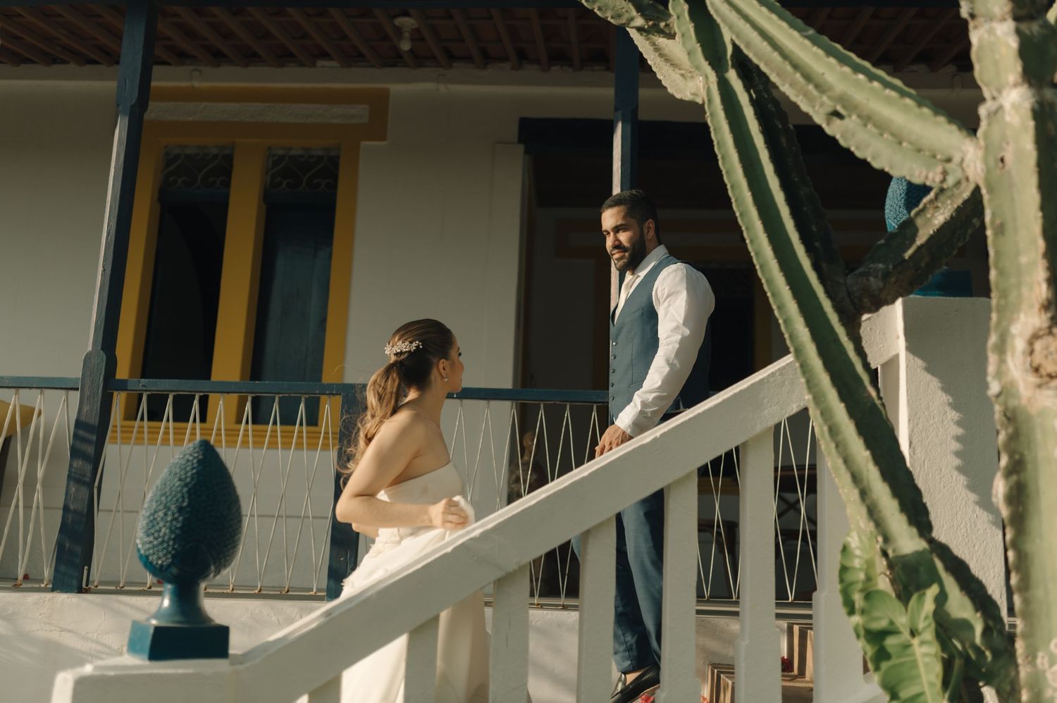 A couple shares a tender moment on a white porch with decorative arches and greenery.