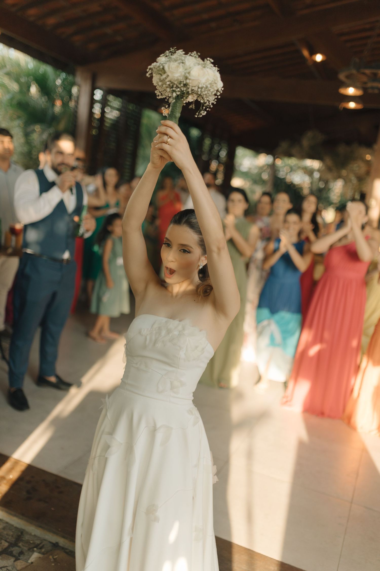 A bride raises her bouquet triumphantly during the wedding reception as guests cheer.