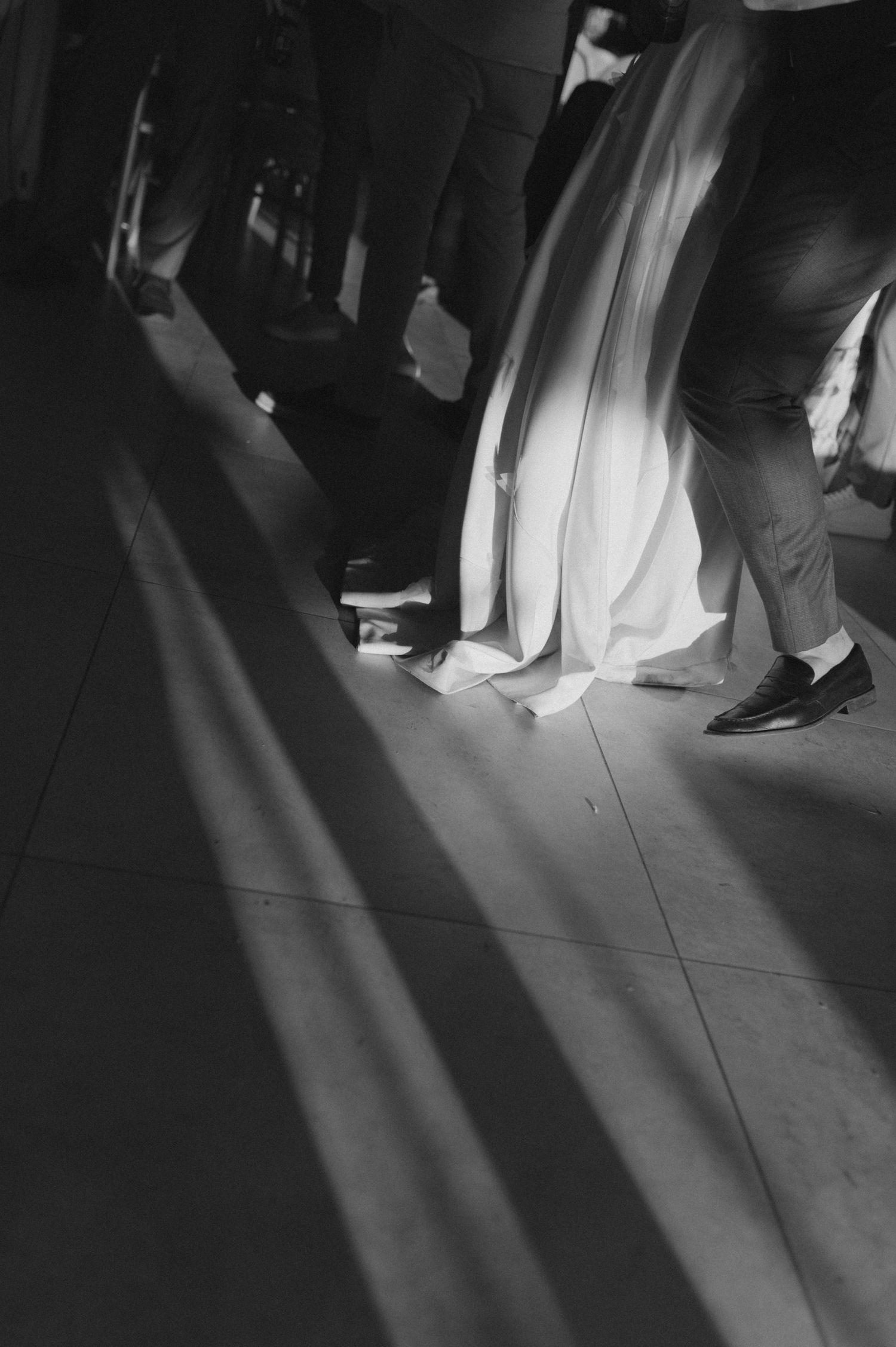 A dramatic black and white photo showing shadows and wedding attire details on a dance floor.