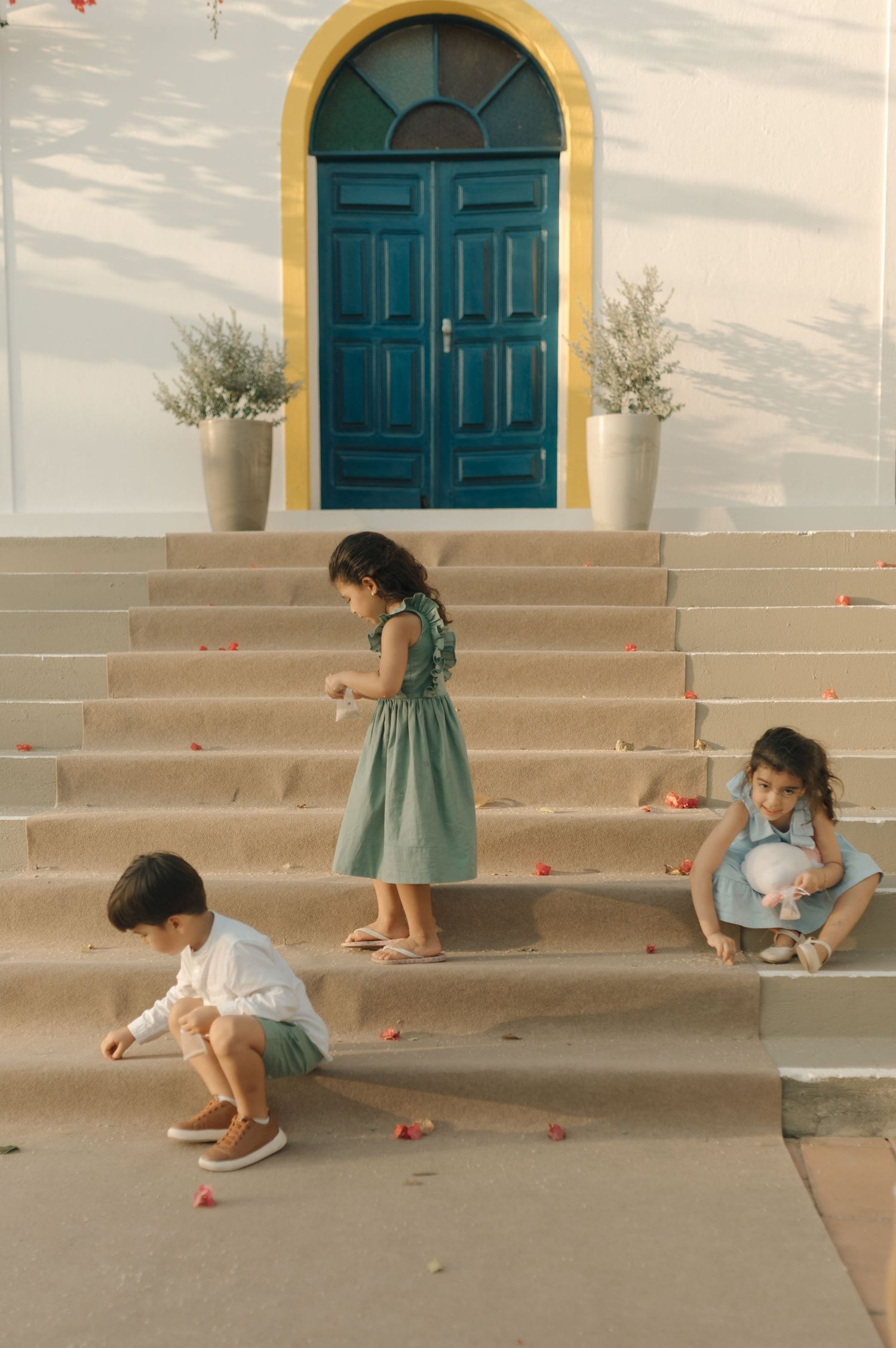 Children play on stone steps leading to a turquoise arched door on a white building.