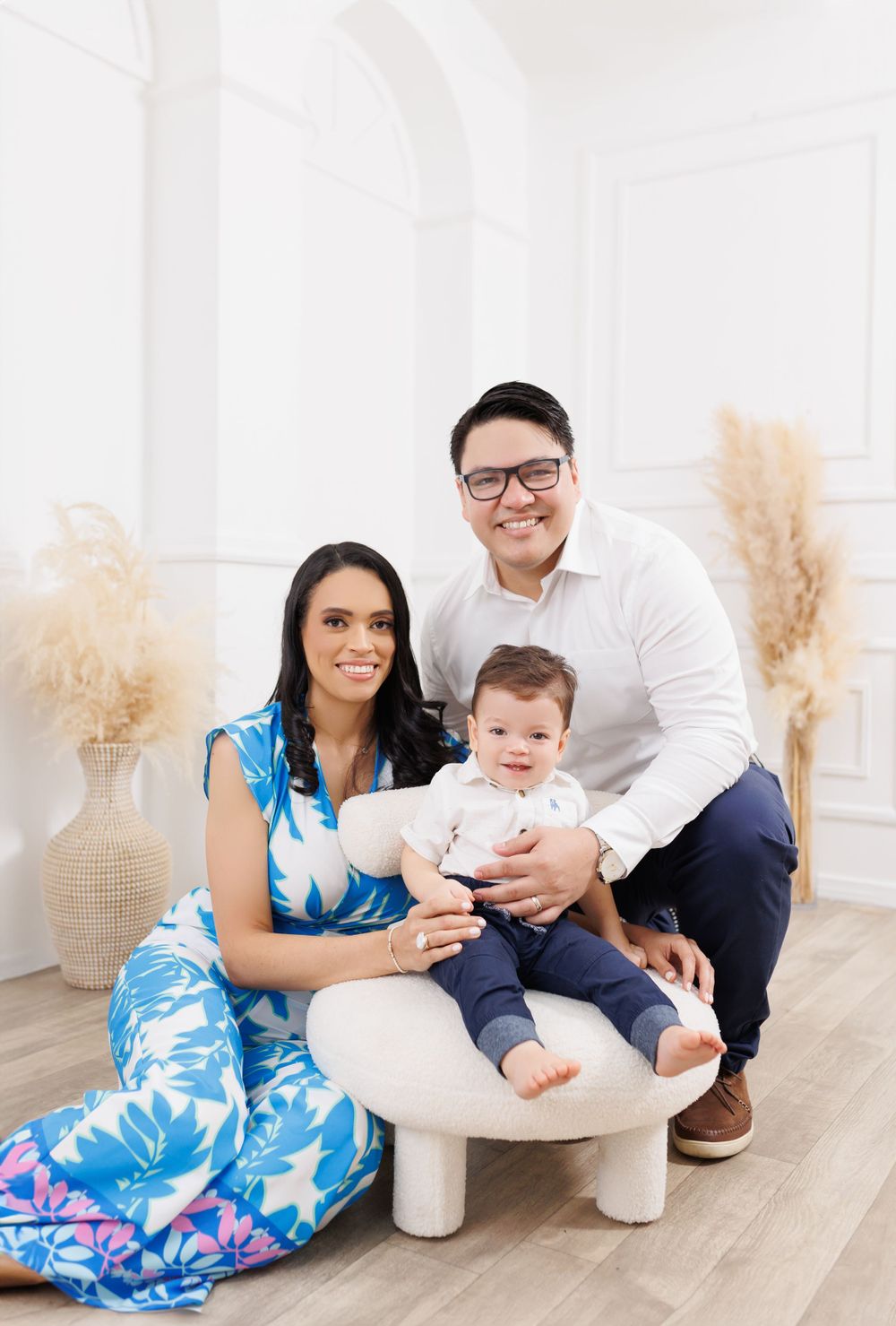 A family sits together on a white bench with pampas grass decor in the background.