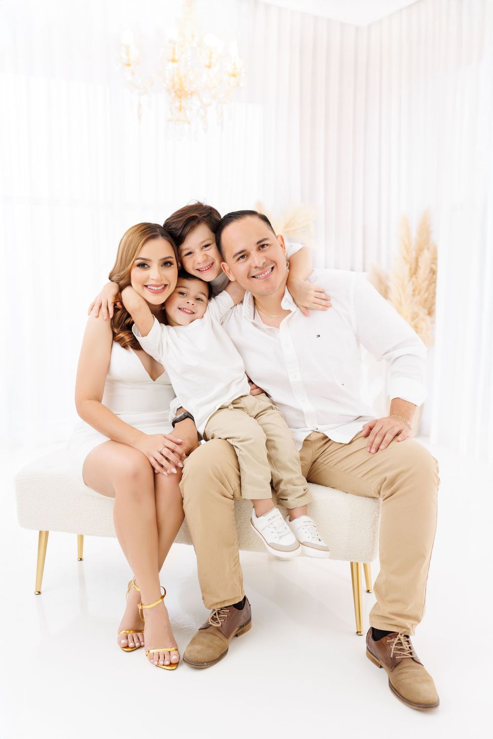 Family portrait in white outfits with gold accents against light background.