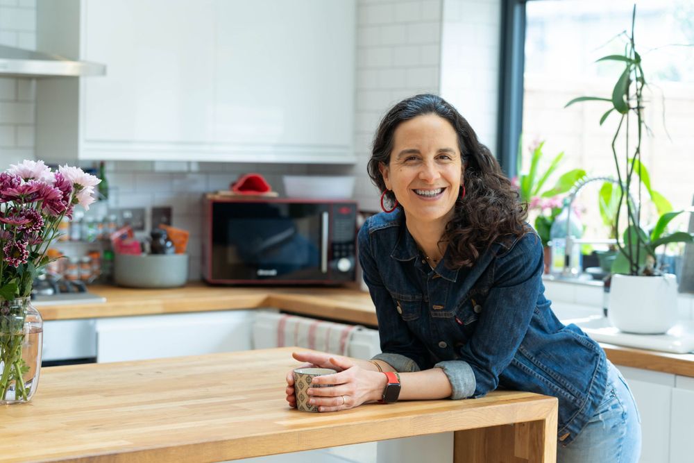 confidence coach leans in her kitchen smiling and holding a cup of tea in her personal branding shoot brighton