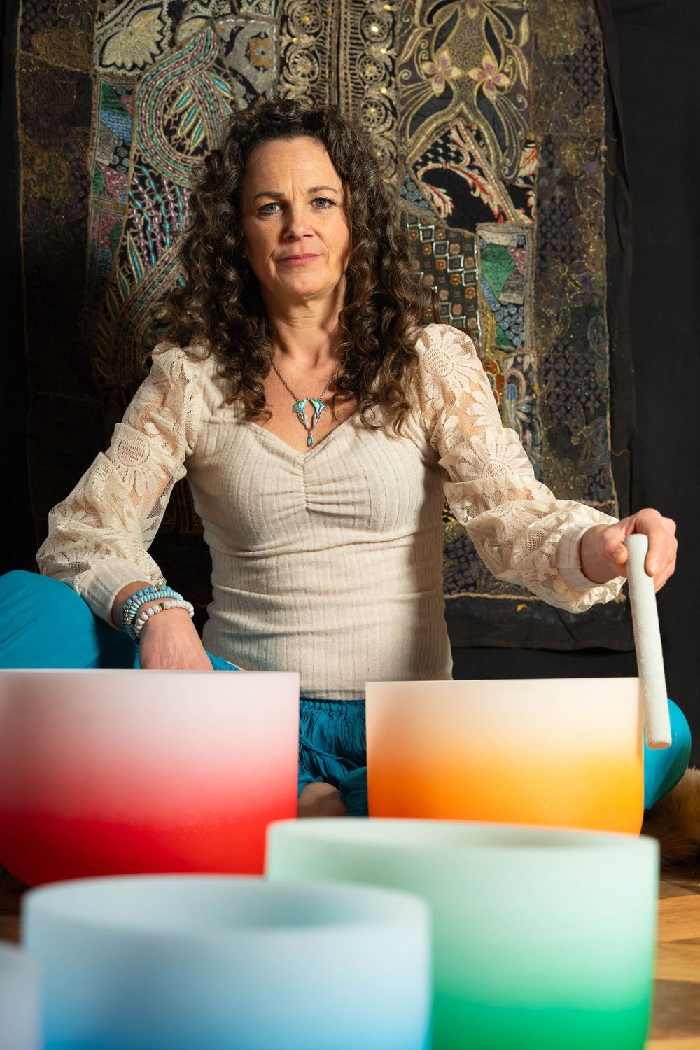 women sound healer in wooden yurt playing colourful crystal bowls