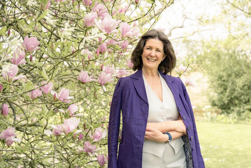 personal branding shoot of a Woman wearing purple jacket over her shoulders stands next to a magnolia tree in a garden