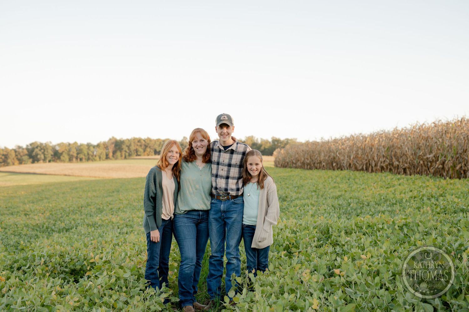 A family stands together in a lush farm field with crops visible in the background.