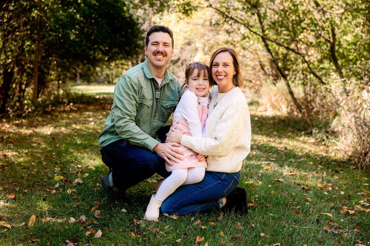 Happy family of three sitting together outdoors on grass in autumn sunlit setting in Novi Michigan by Rachel Martinez Photography