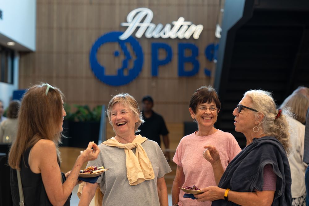 Four women laughing and socializing at an Austin PBS event inside the station lobby.