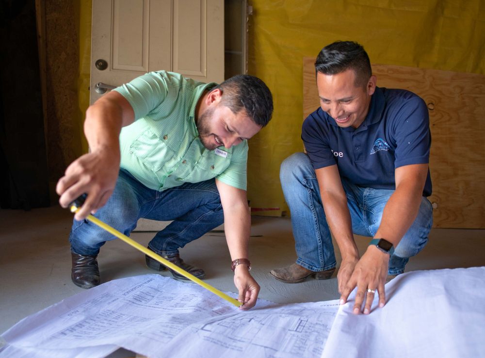 Two construction professionals reviewing blueprints together while crouching on the floor.