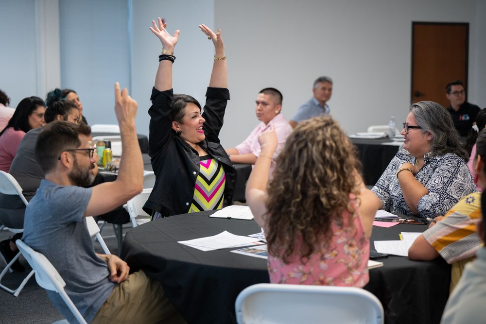 Enthusiastic participants raise their hands during an interactive workshop session at round tables.