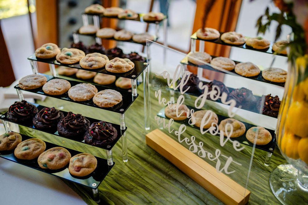 Tiered display of freshly baked chocolate chip and dark chocolate cookies arranged on wooden stands with wine glasses.