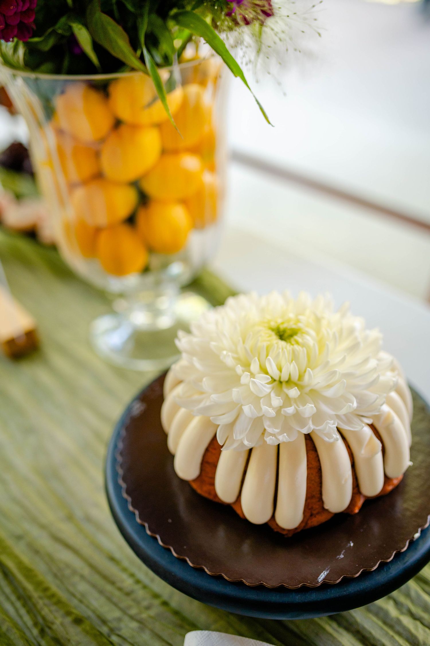A chocolate bundt cake topped with white frosting and a fresh white chrysanthemum flower on a blue plate.