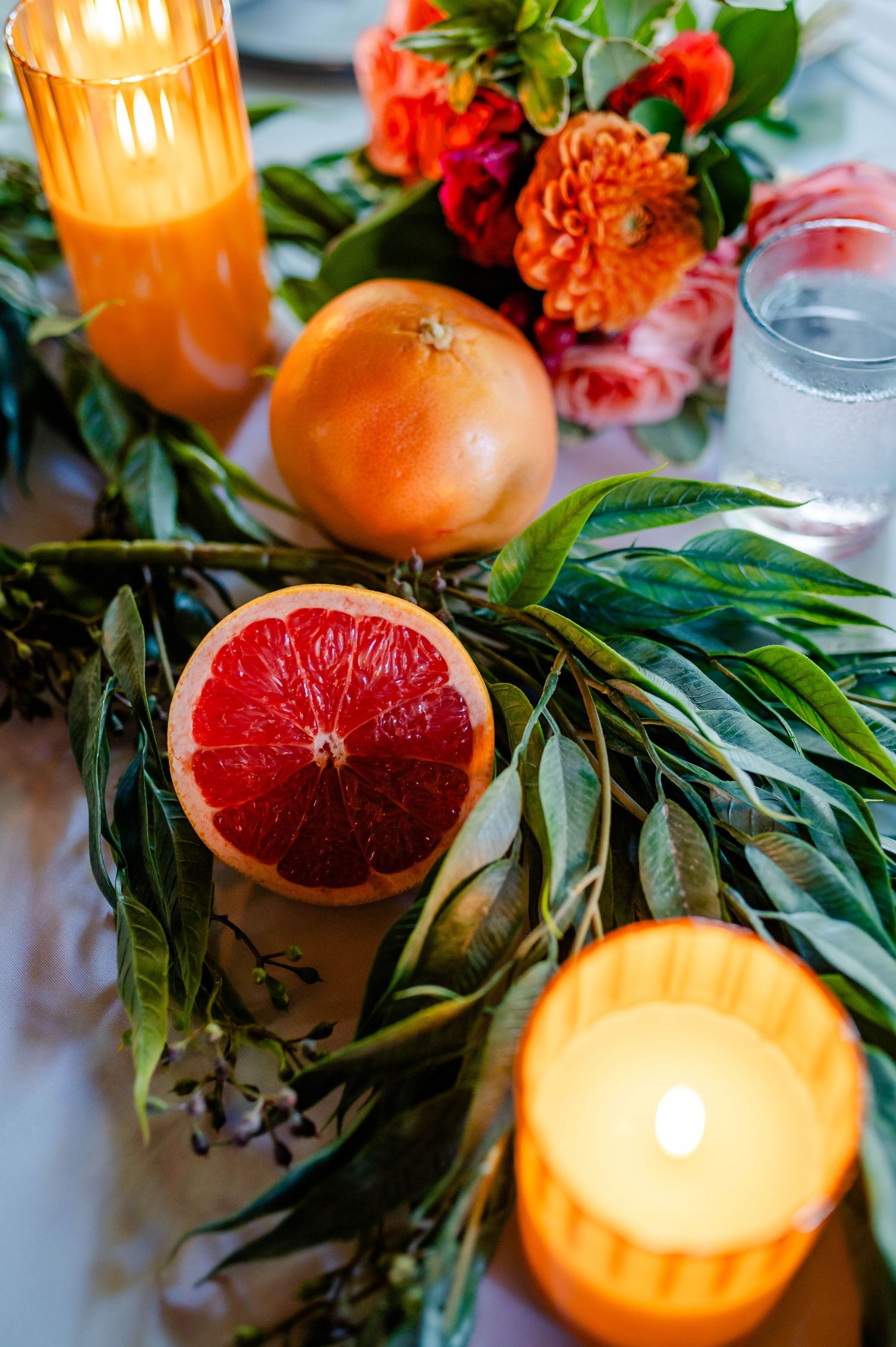 Citrus fruits and greenery arranged with glowing candles create an elegant table setting.