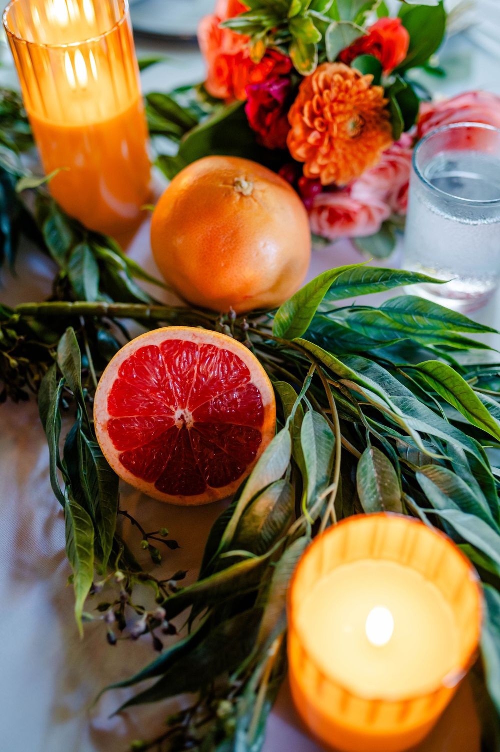 Citrus fruits and greenery arranged with glowing candles create an elegant table setting.