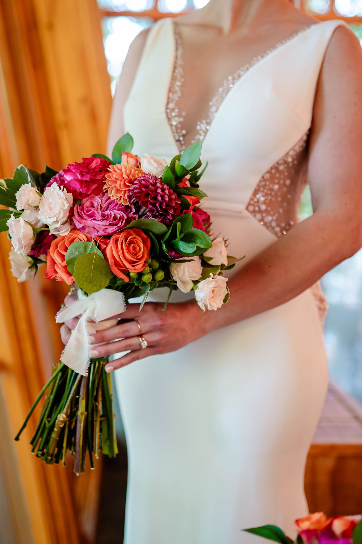 Close-up of a bride holding a vibrant bouquet with pink, orange and white flowers against her white wedding dress.
