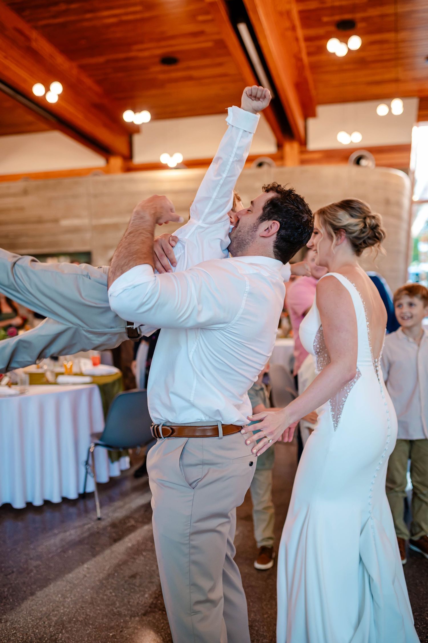 Wedding couple shares playful dips across a reception dance floor with elegant white decor and warm lighting.