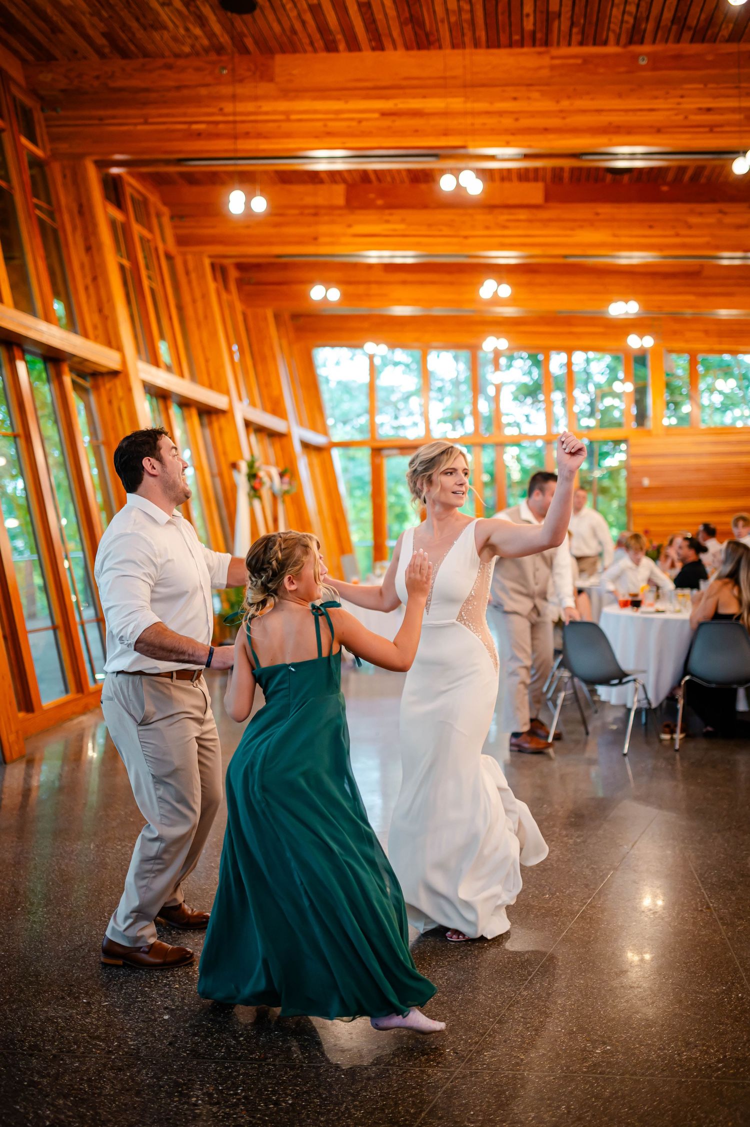 Wedding party members perform synchronized dance moves in elegant wooden reception hall.