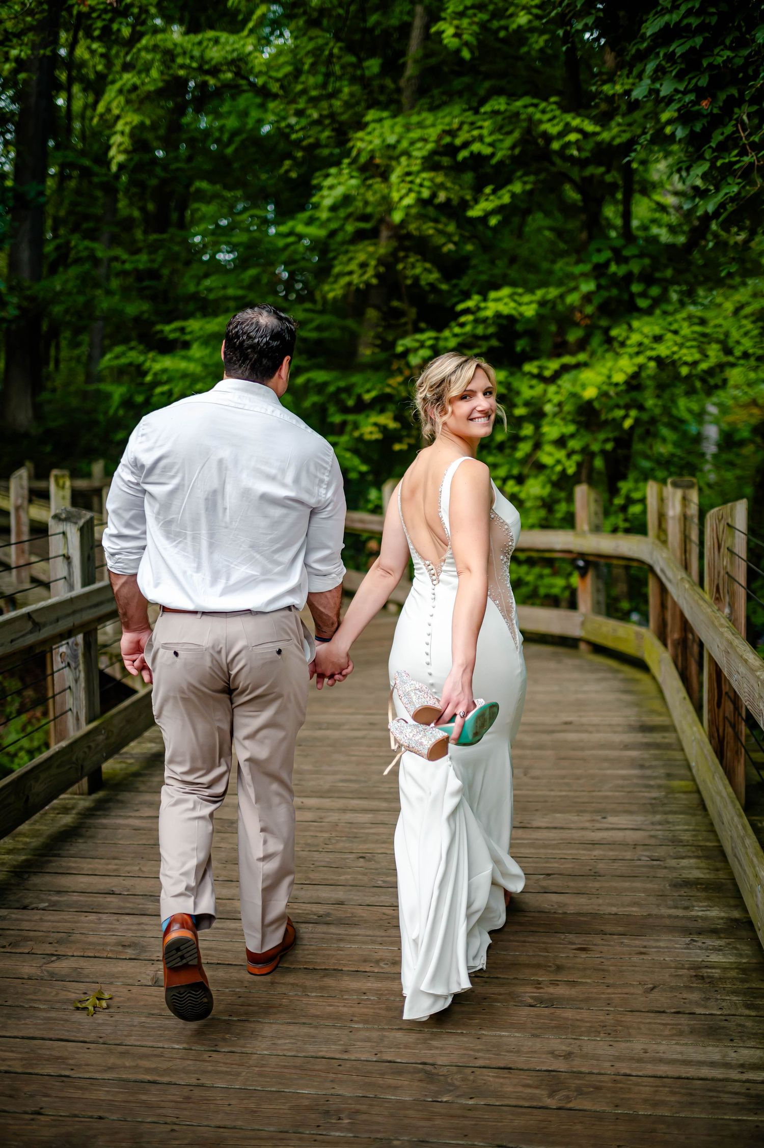 A romantic couple walking along a wooden boardwalk surrounded by lush green foliage.
