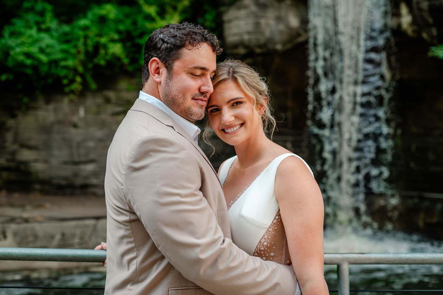 A bride and groom share intimate moments against a stone wall backdrop during their outdoor wedding celebration.