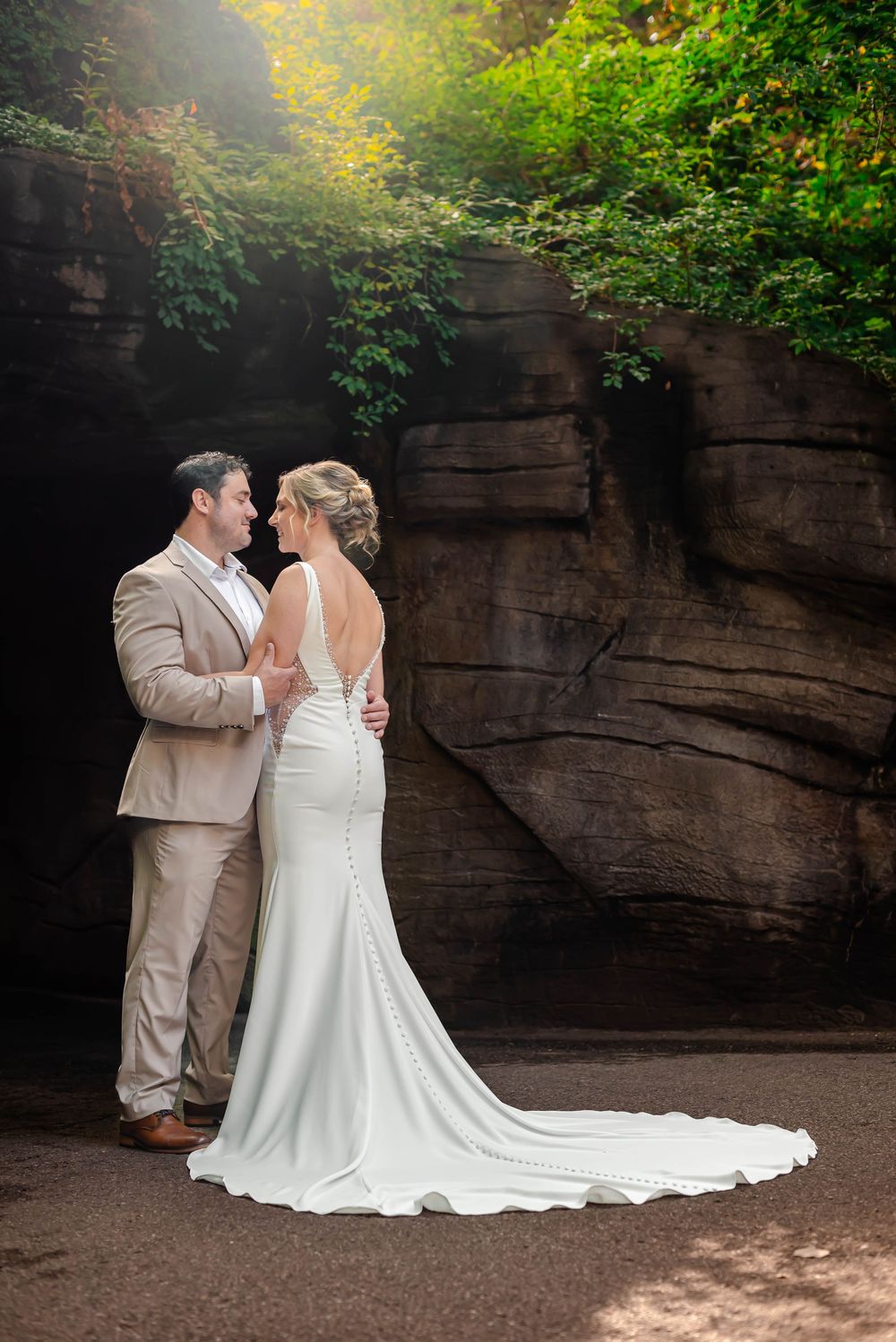 A couple in formal attire share a romantic moment against a rocky cliff backdrop.