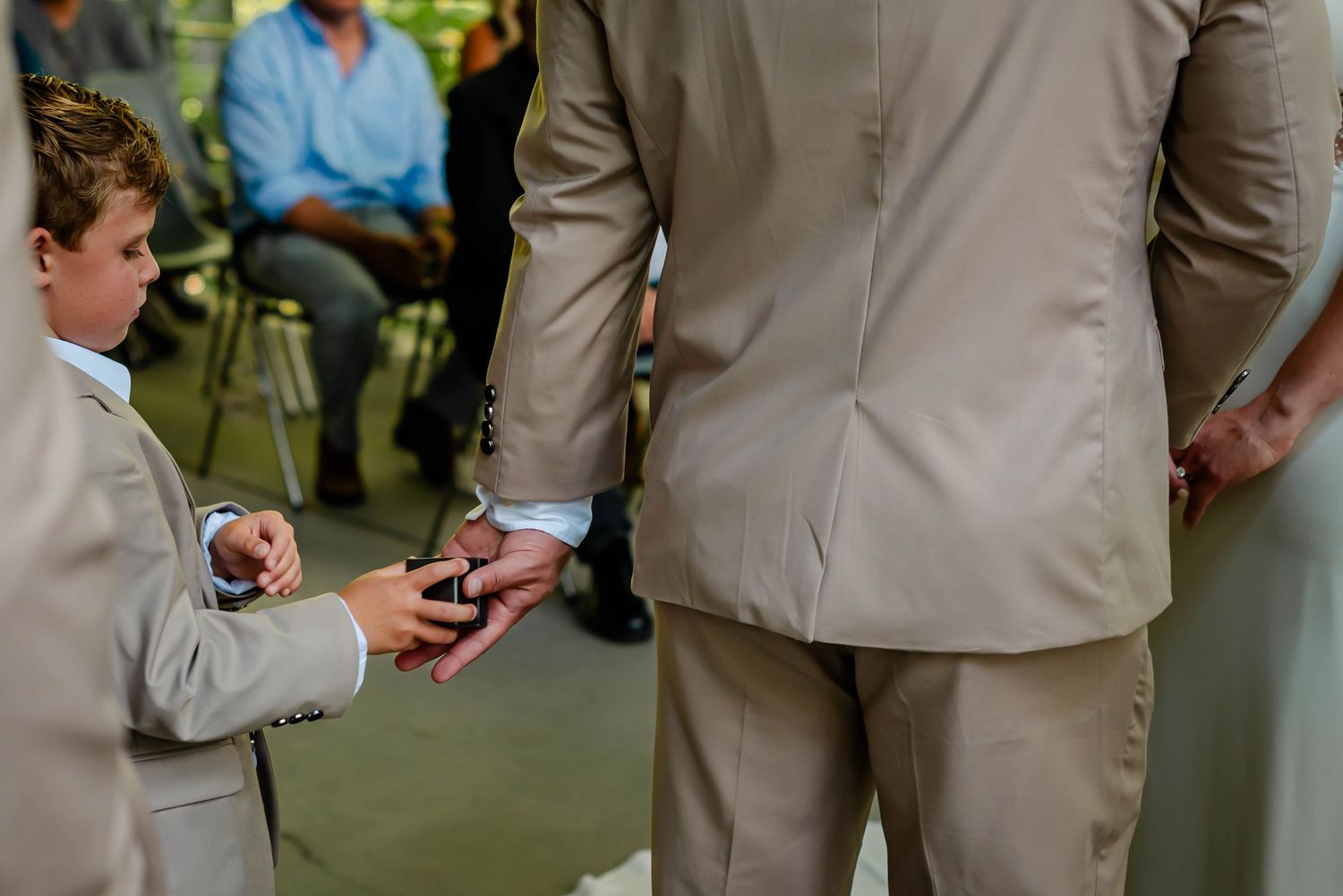 Groomsmen in beige suits stand holding refreshments at an outdoor wedding reception.