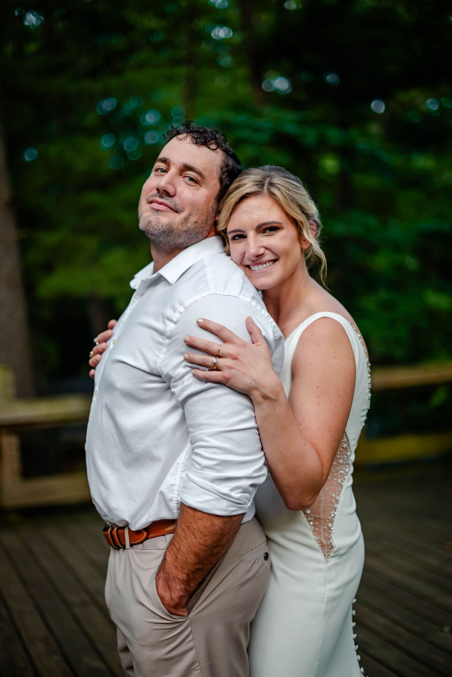 A joyful couple sharing laughter and embraces on a wooden deck in a forest setting.