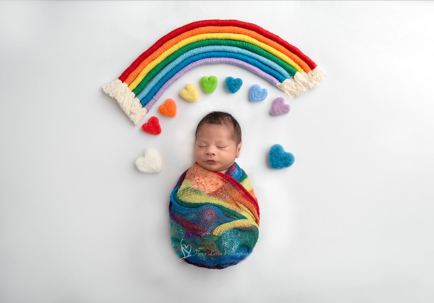 Colorful rainbow art arrangement with newborn wrapped in rainbow swaddle against white backdrop.