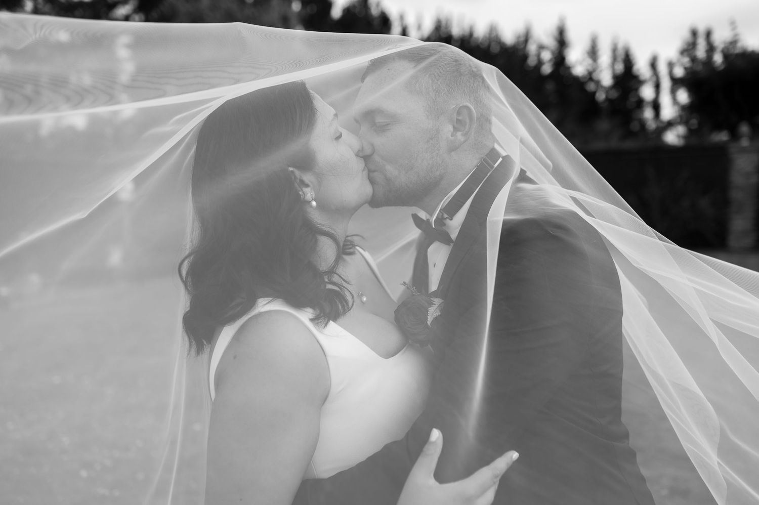 A tender black and white wedding photo sequence showing a couple embracing under a flowing veil during their ceremony.
