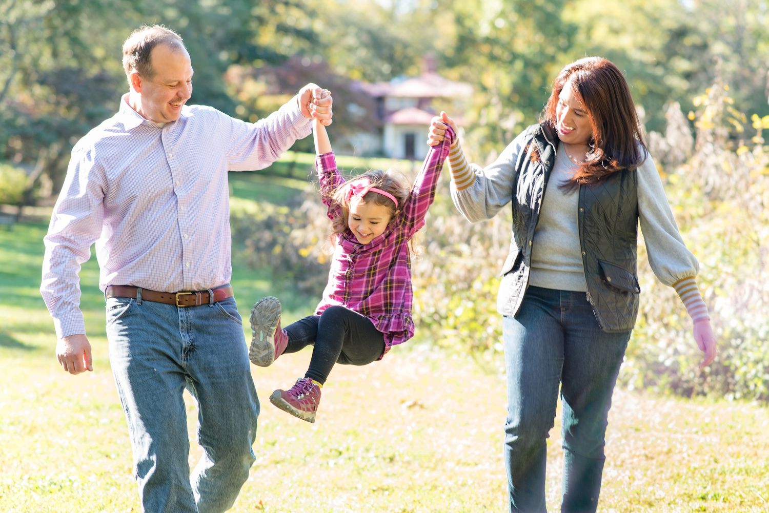 Young girl laughing as parents swing her during a candid family photo session in a park in Northern Virginia