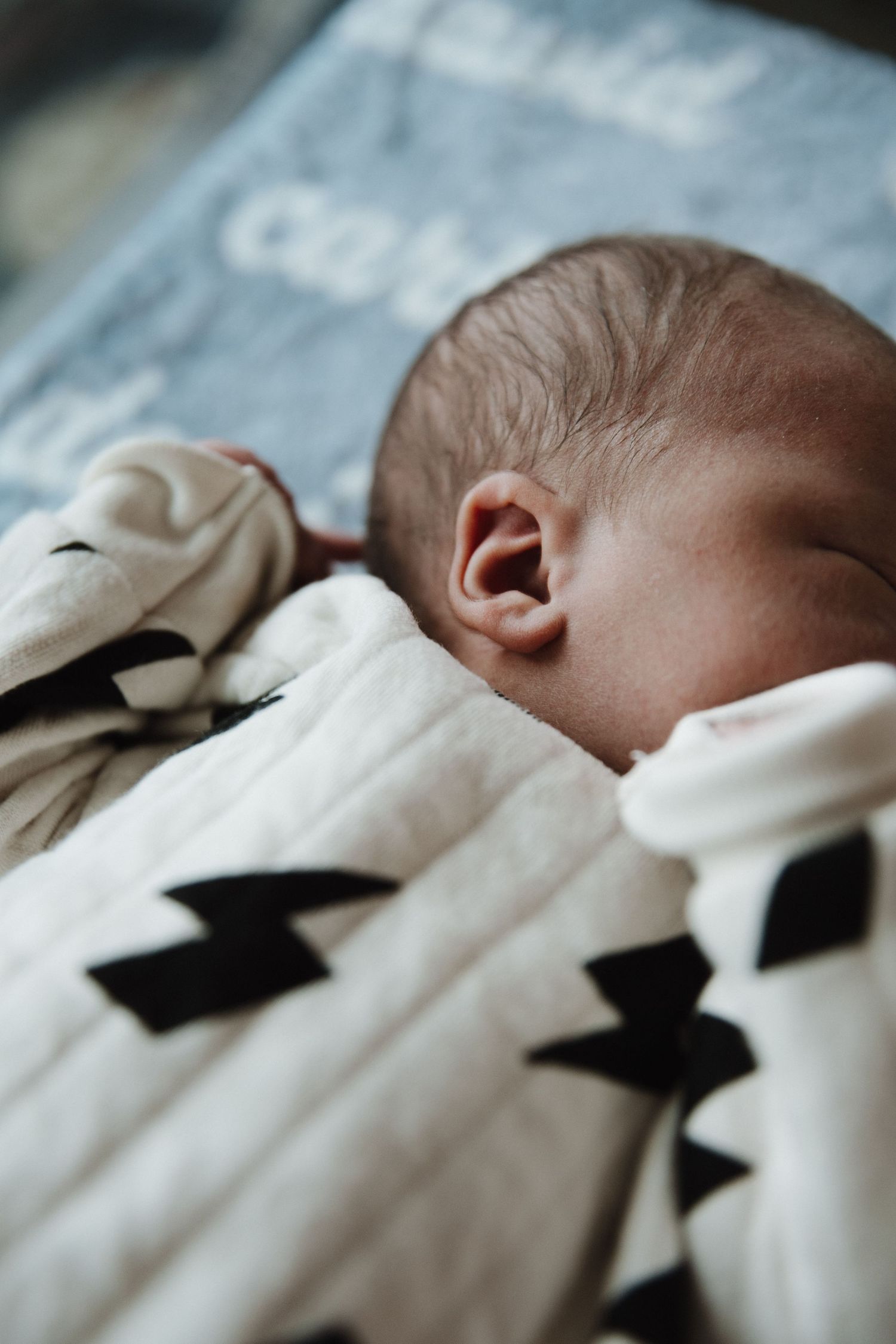 Close-up view of a sleeping baby wrapped in a white blanket with black geometric patterns.