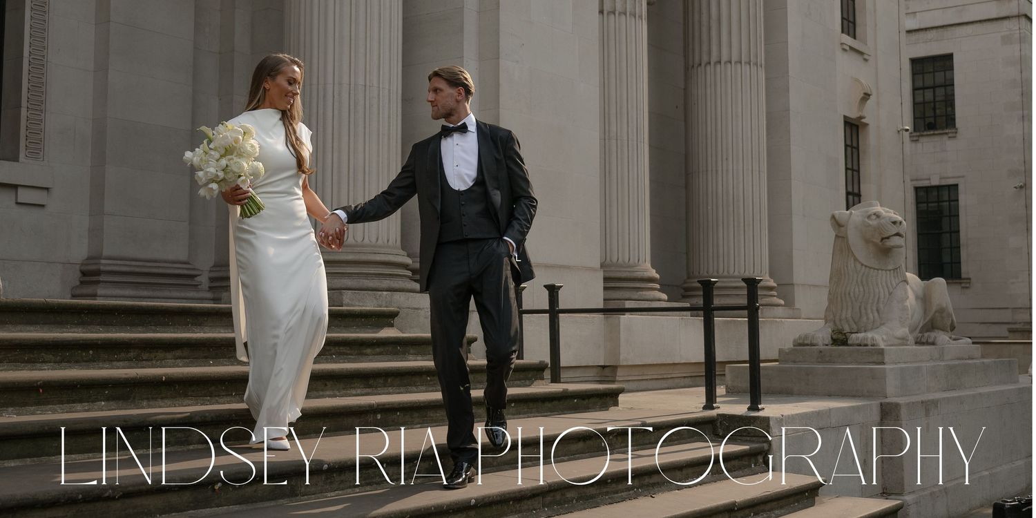 A couple in wedding attire stands together on stone steps outside a grand building with classical columns.