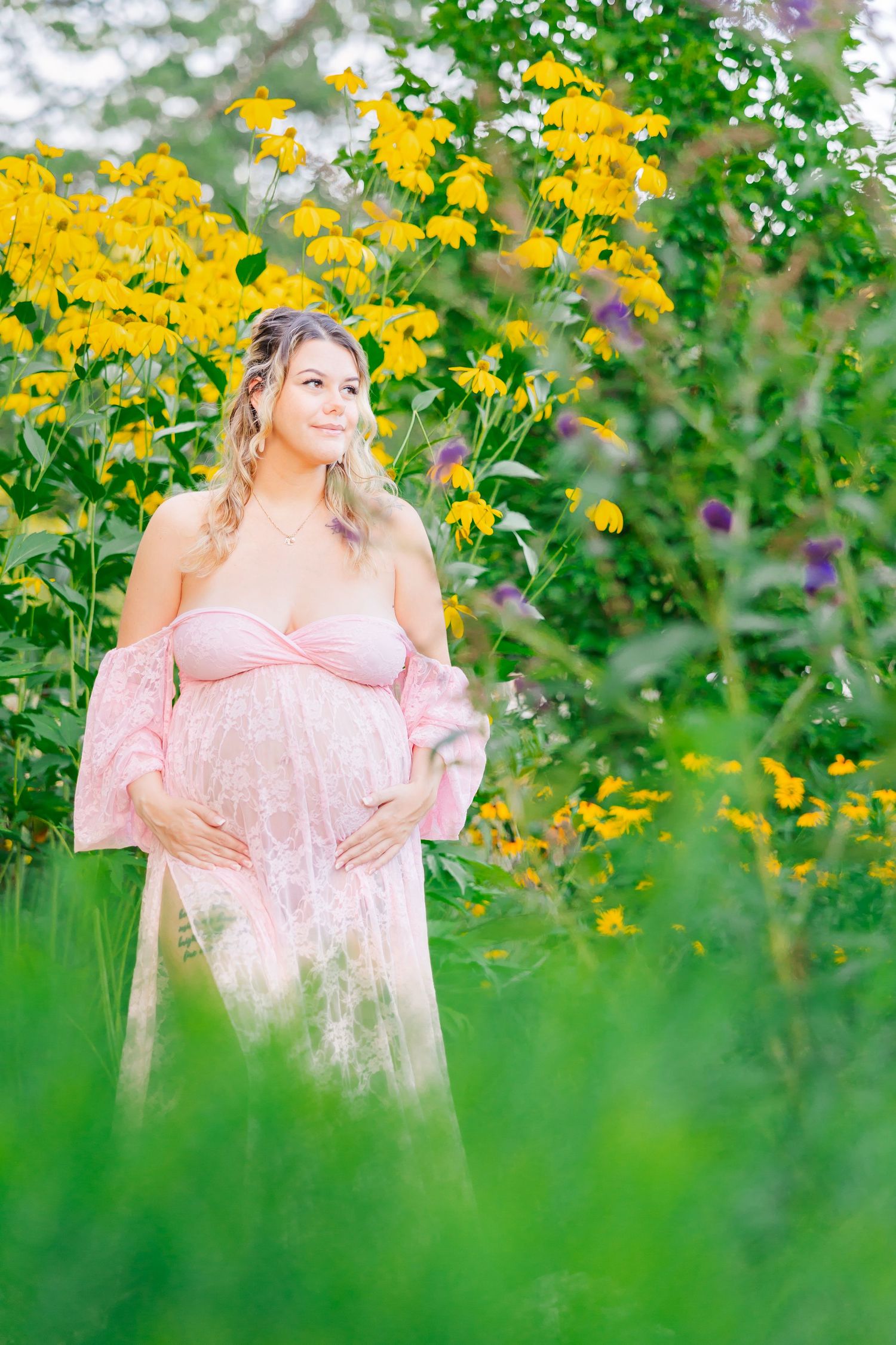 Beautiful maternity photoshoot in a garden with vibrant yellow wildflowers and soft pink dress creating a dreamy scene.