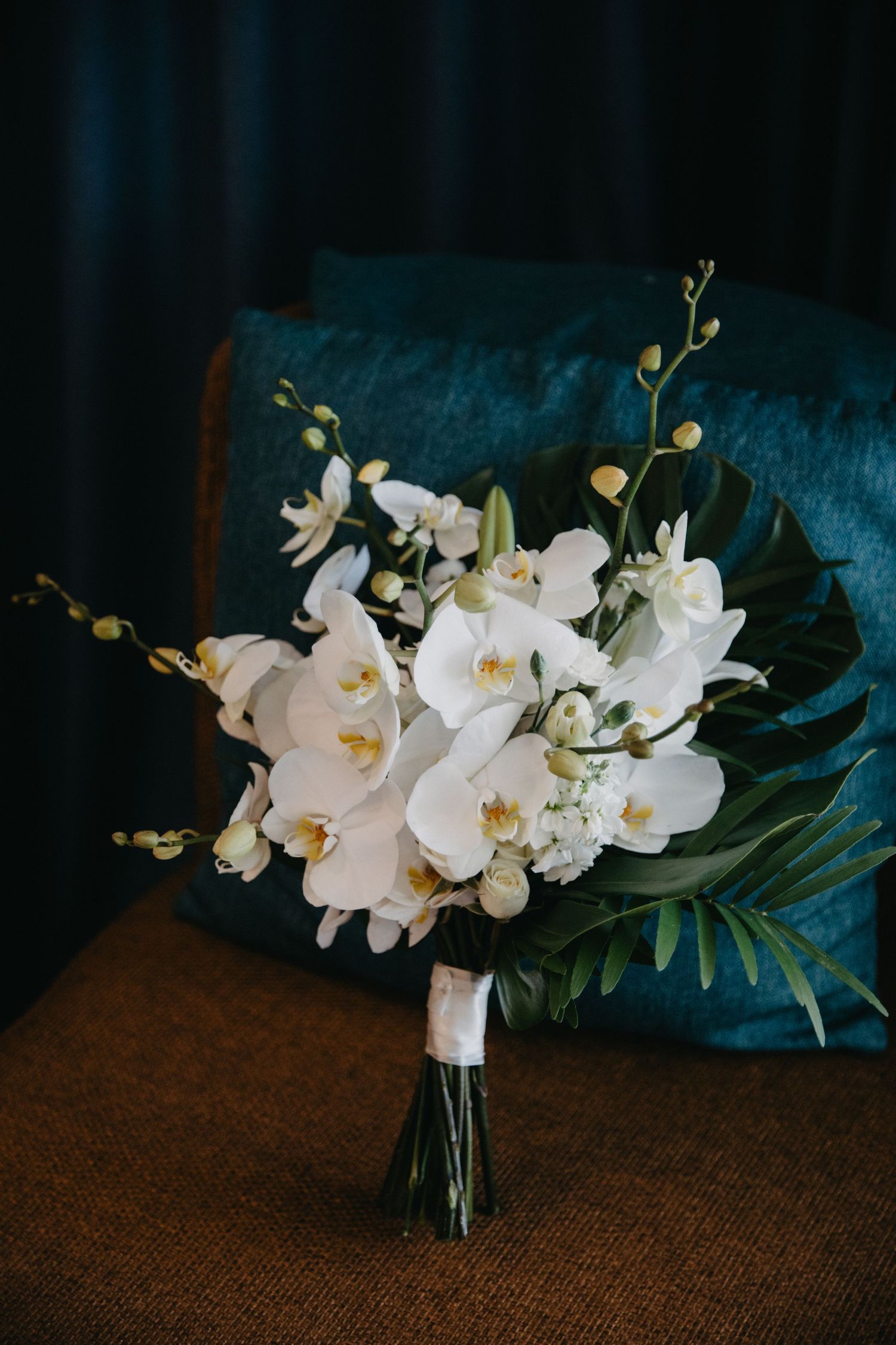 Elegant white orchid and floral wedding bouquet against a deep teal velvet background.
