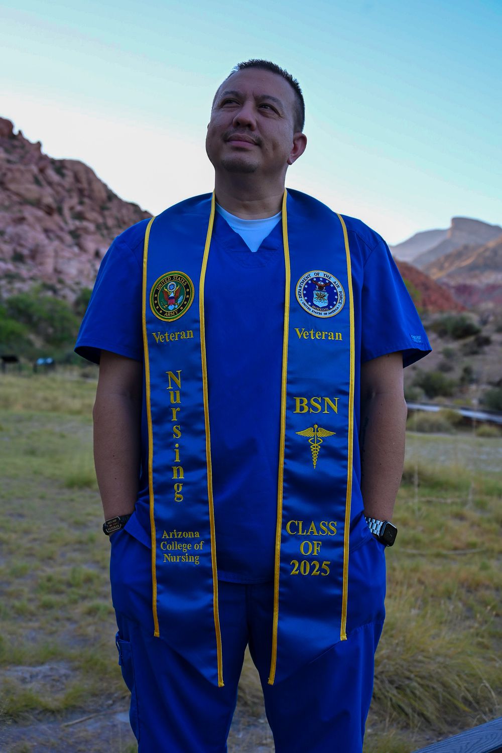 Veteran nursing graduate in blue scrubs and gold BSN Class of 2025 stole poses outdoors.