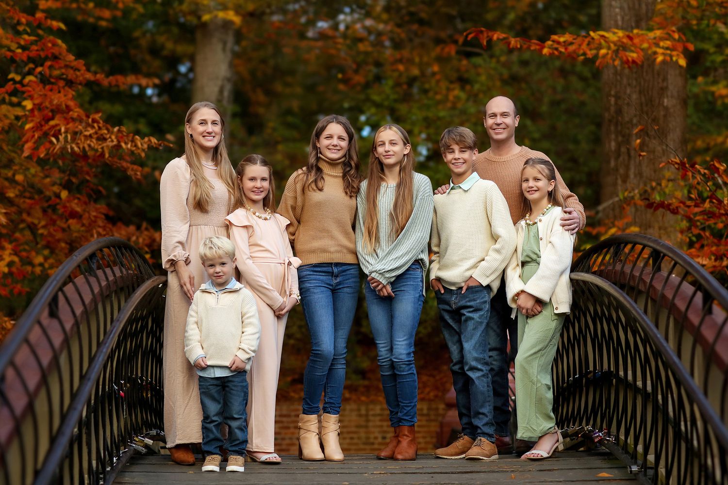 A group of people pose for autumn family photos on a rustic bridge surrounded by vibrant orange fall foliage.