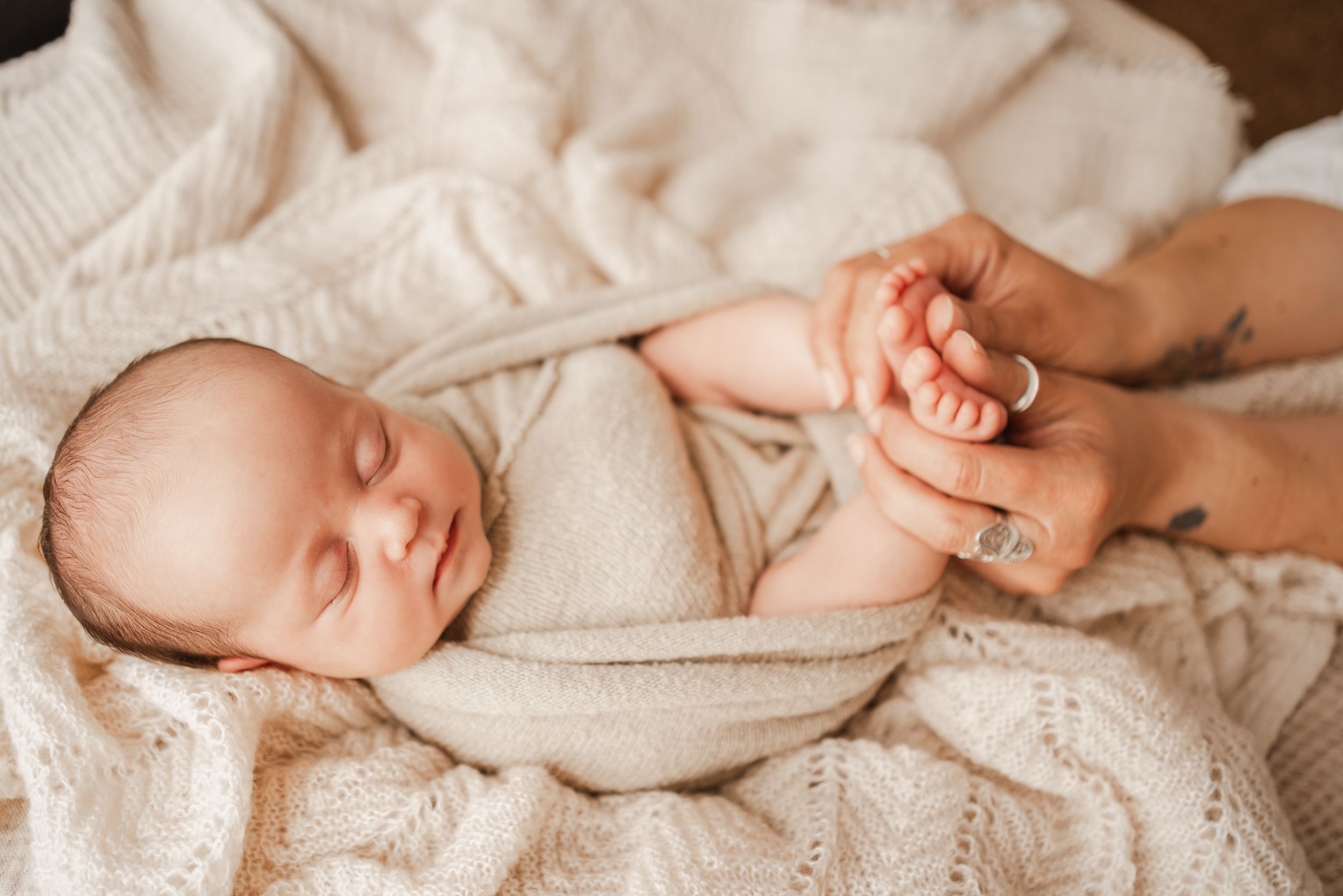Newborn baby wrapped in soft blankets at home in Portland Dorset with grandmother gently holding her tiny feet