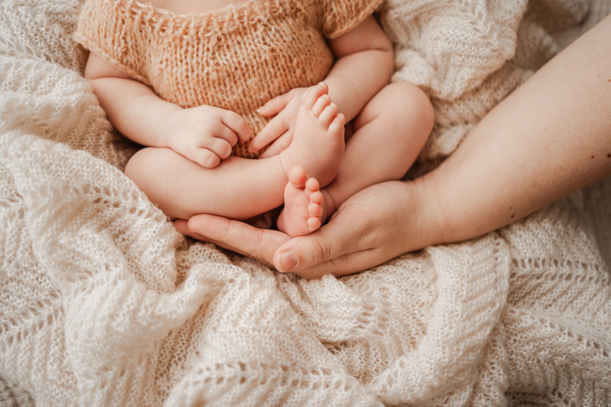 Close-up of newborn baby feet in knitted romper during cosy in-home session in Portland, Dorset with soft natural light.