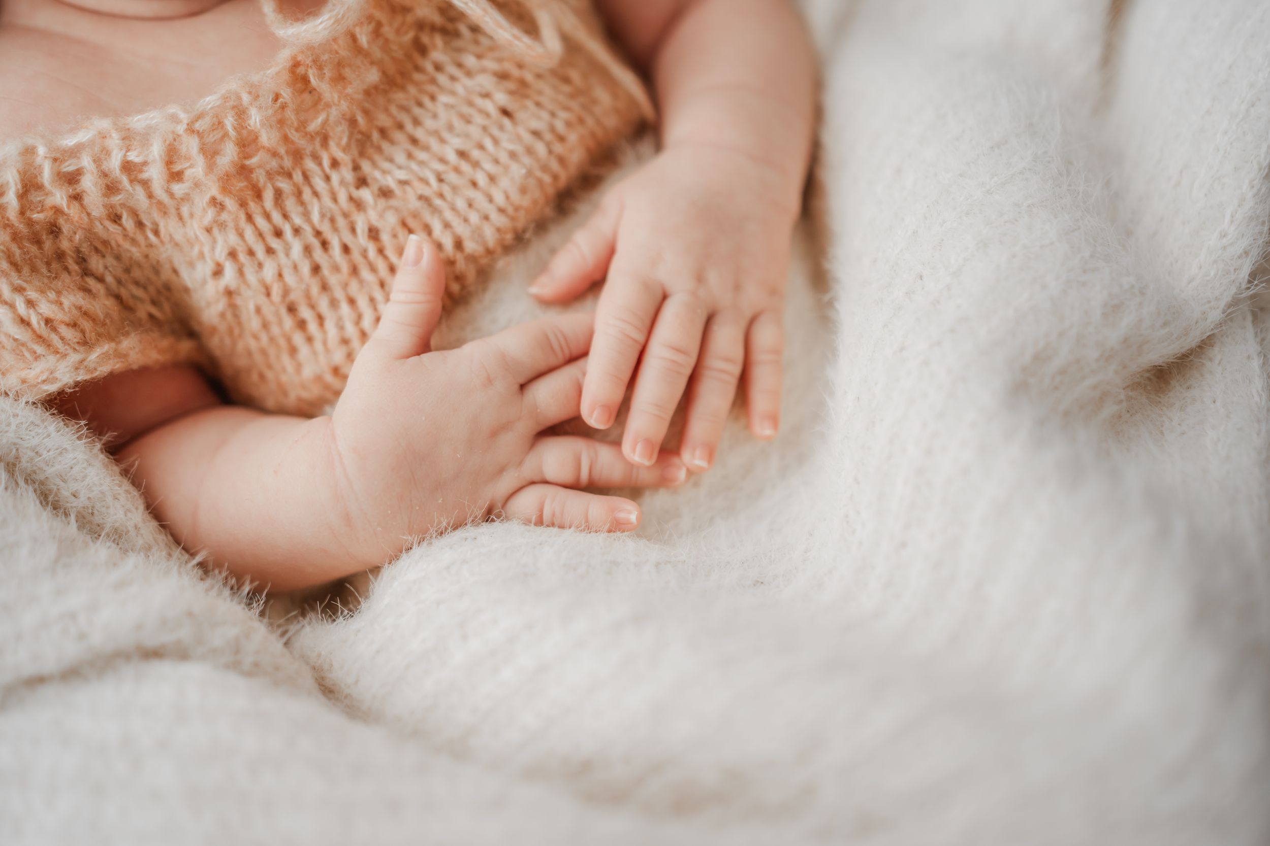 Close-up of newborn baby's hands on knitted romper during Portland, Dorset in-home newborn photography session.