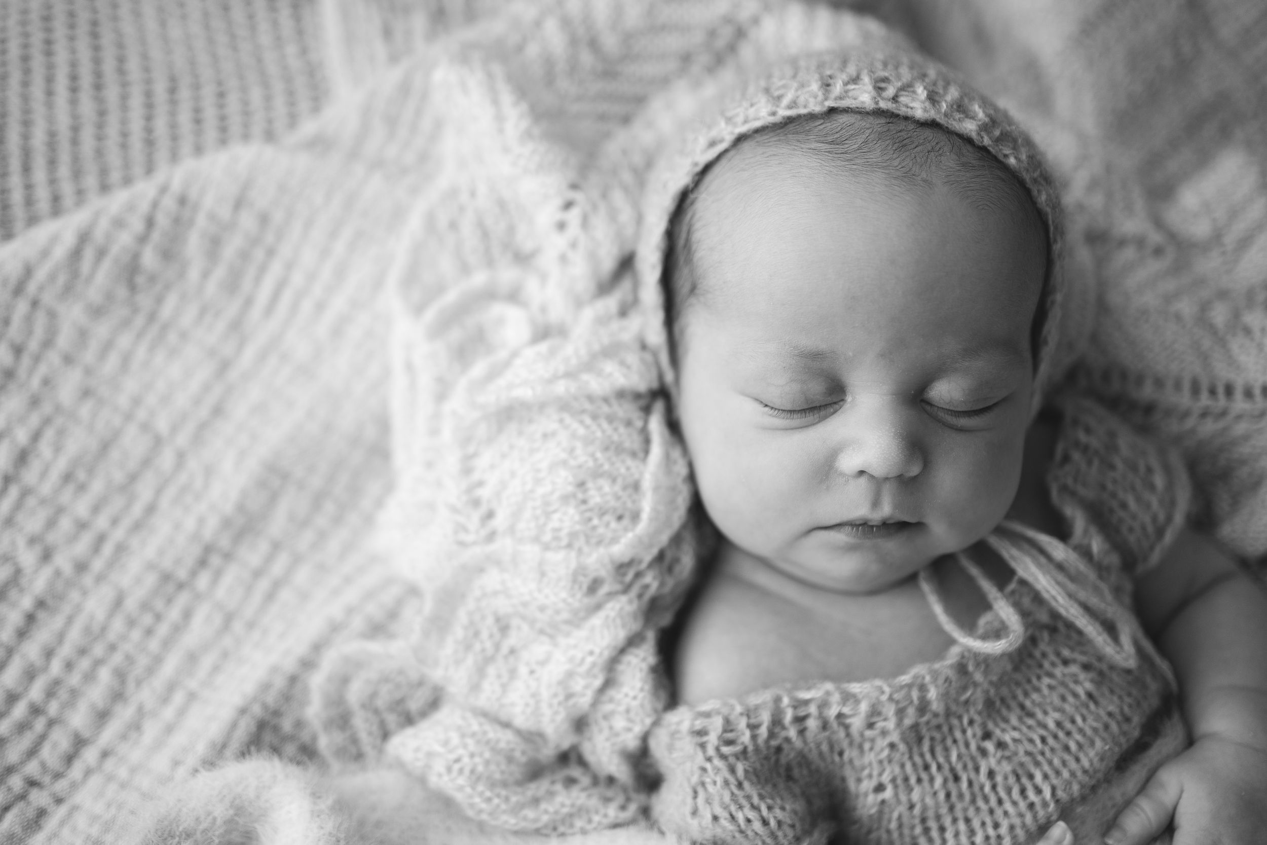 Newborn baby girl sleeping peacefully in knitted bonnet and romper during in-home session in Portland, Dorset