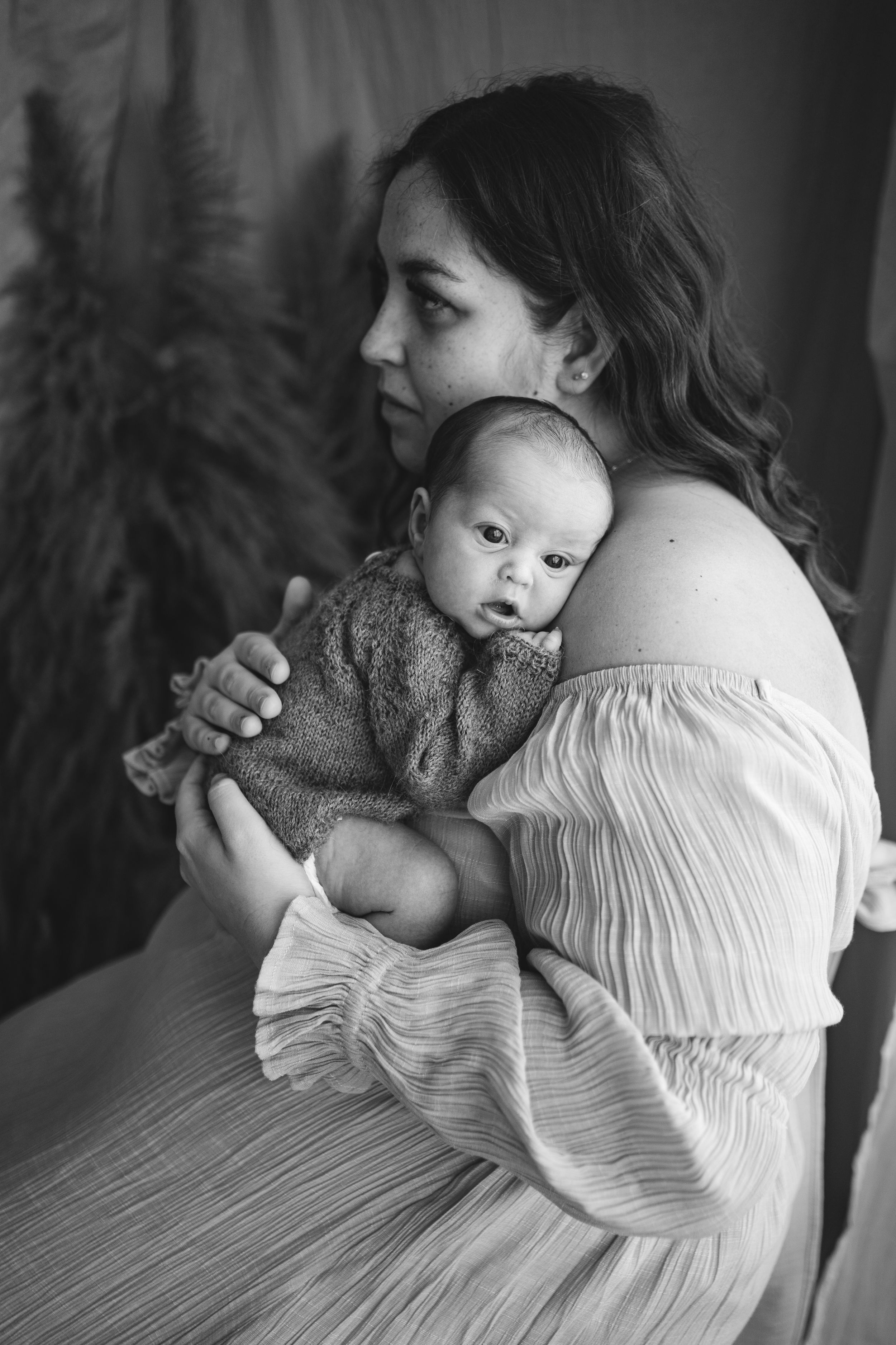 Close up of a wide-eyed newborn baby held against her mother's shoulder during an in-home newborn photography session on Portland, Dorset.