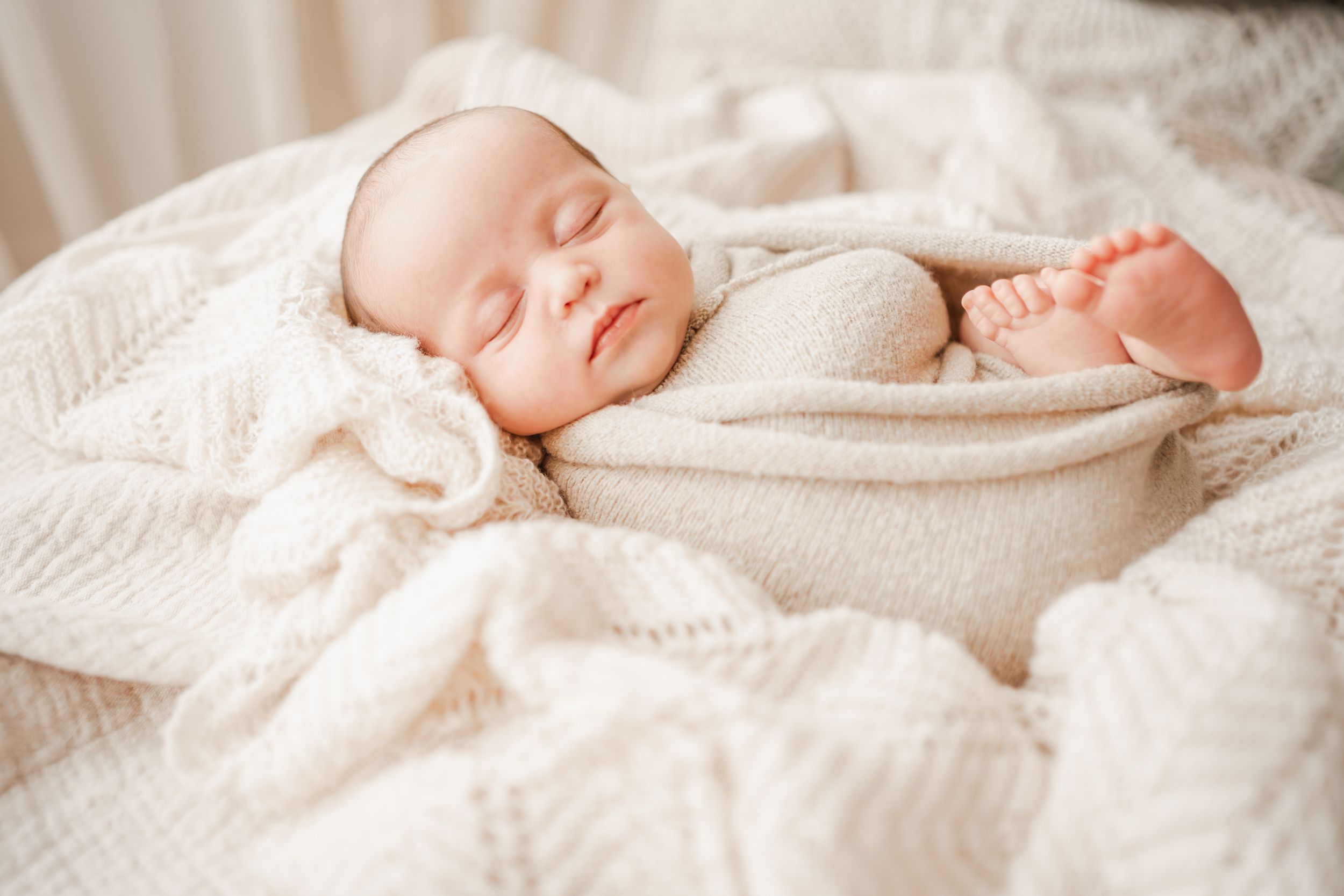 Newborn baby girl wrapped in a neutral blanket sleeping peacefully in during an in-home photo shoot on Portland, Dorset, UK