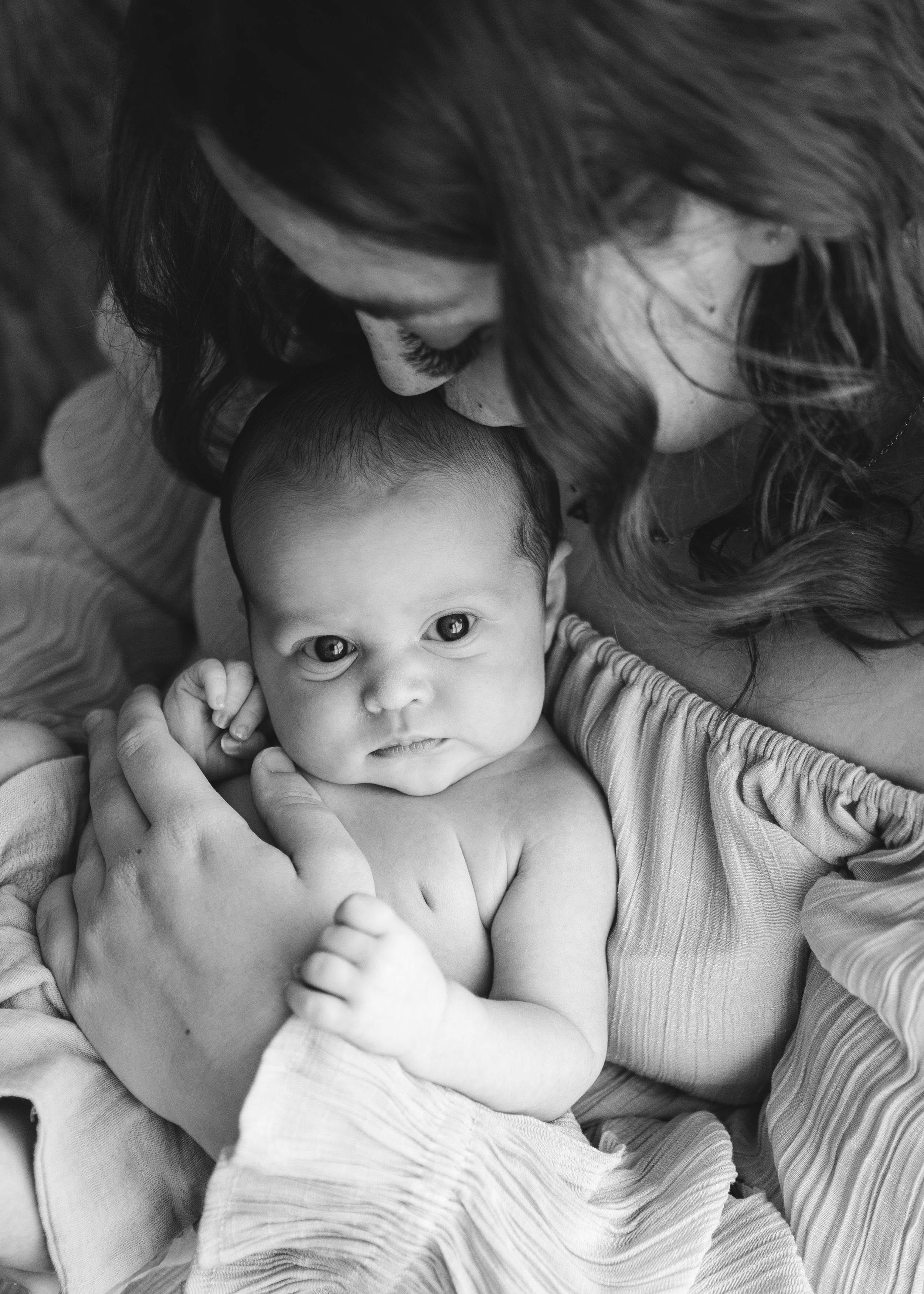Three week old baby girl in Portland Dorset held close during in-home newborn session, eyes wide open and full of wonder.