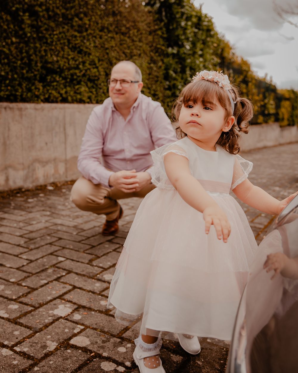 A white dress-clad child stands on cobblestones during an outdoor celebration.