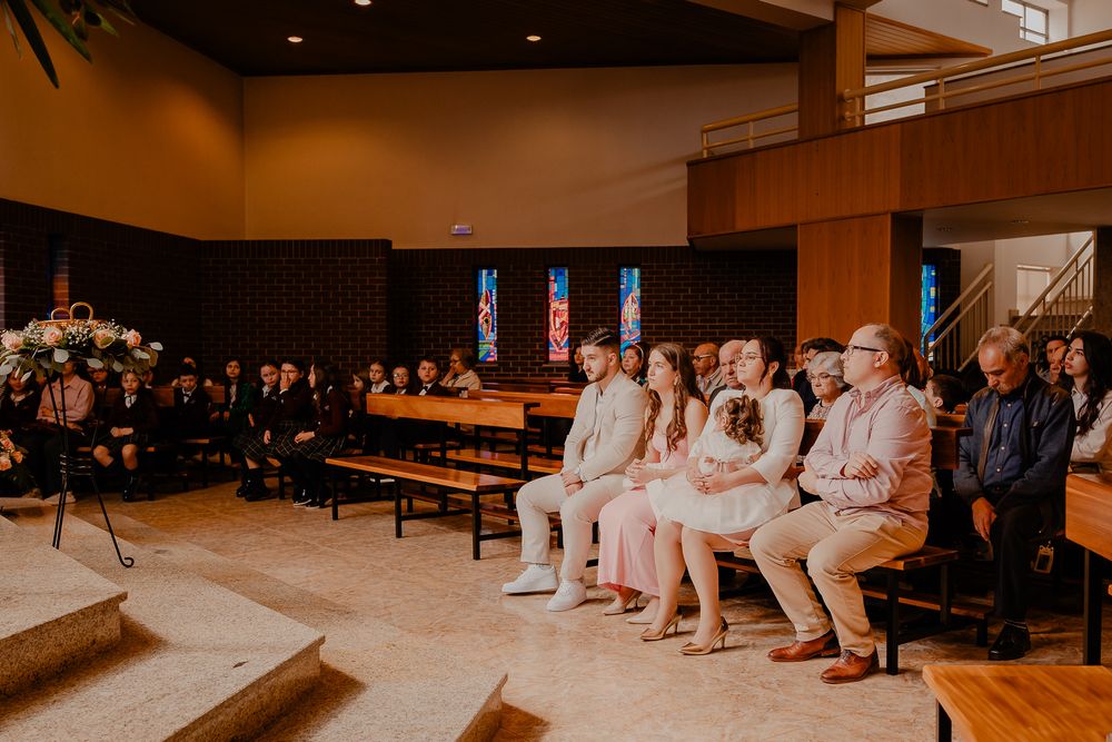 Wide view of a church ceremony with guests seated in wooden pews.